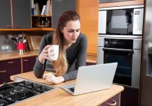 Une femme se tient derrière son écran d'ordinateur avec une tasse à café dans la main