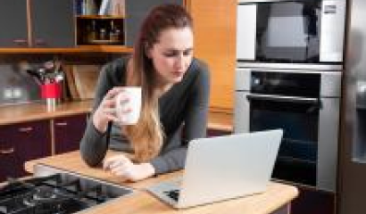 Une femme se tient derrière son écran d'ordinateur avec une tasse à café dans la main